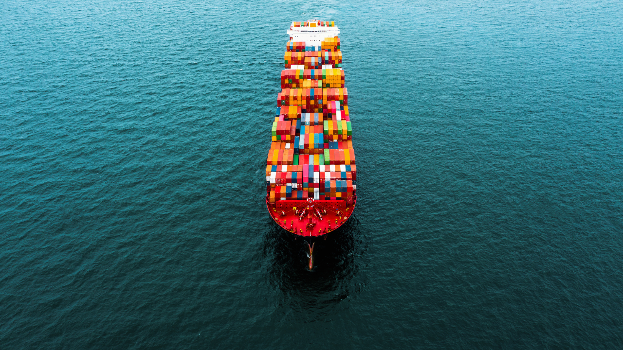 red ship with many shipping containers of various colors on the open ocean